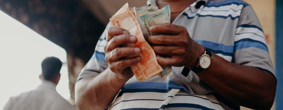 Indian man in a blue-and-white striped polo shirt holding banknotes