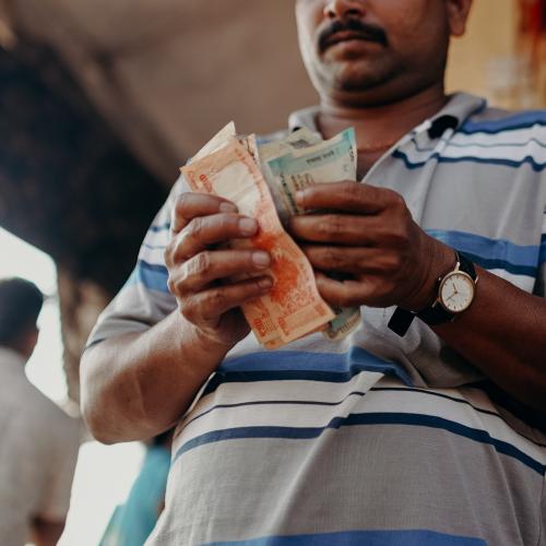 Indian man in a blue-and-white striped polo shirt holding banknotes